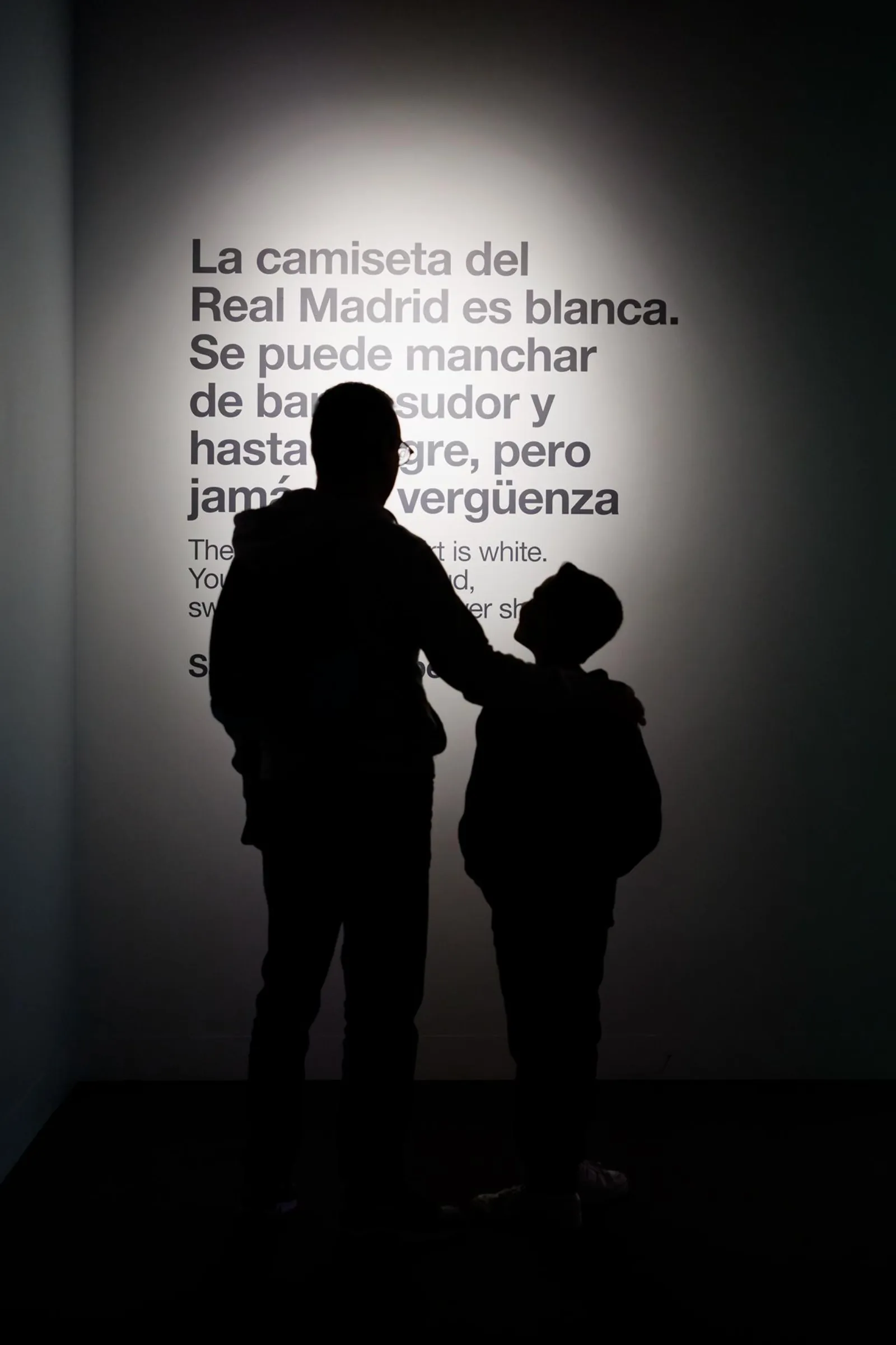 Visitors silhouetted in the Real Madrid museum beside a wall of club history text