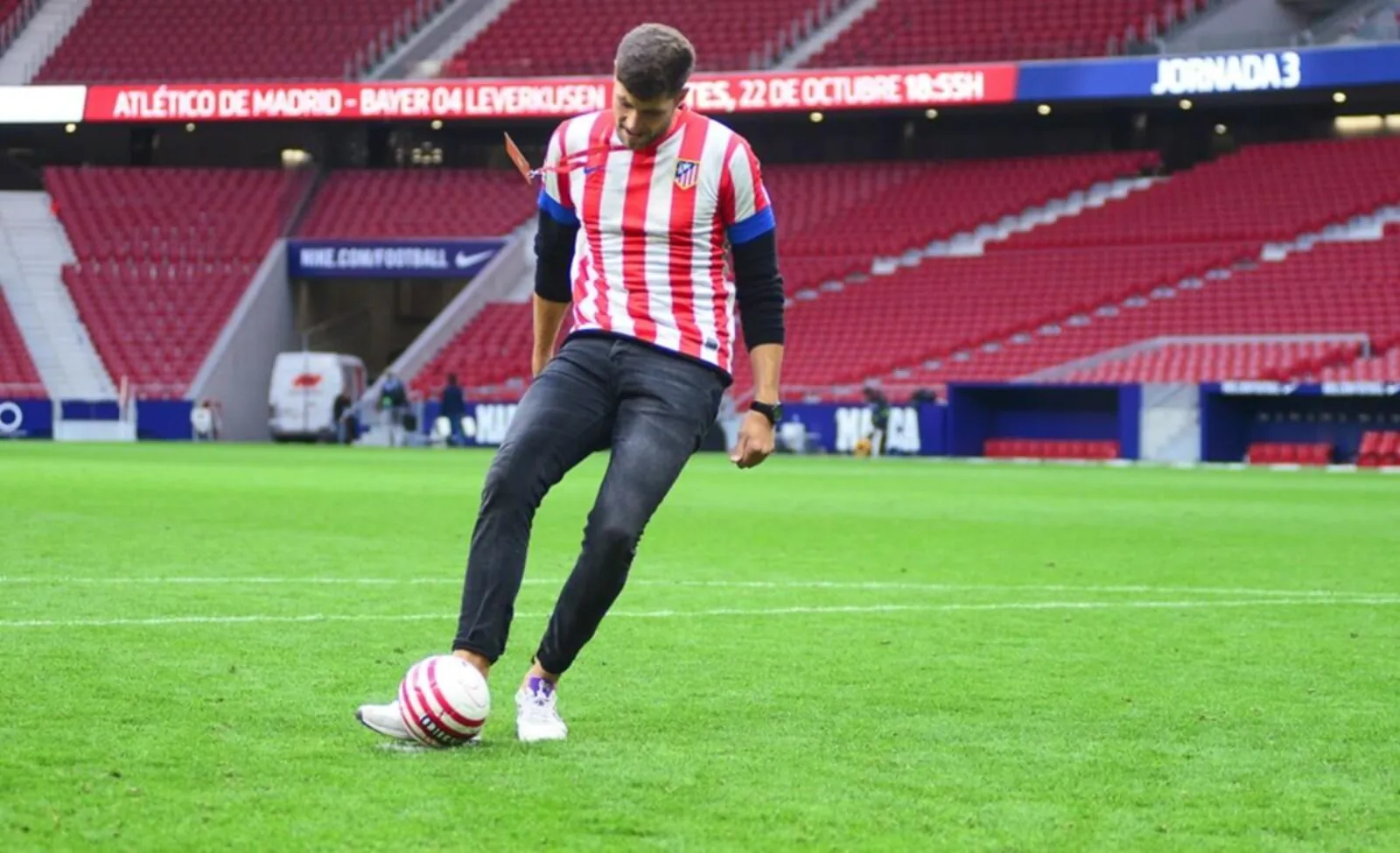 Fan in an Atlético shirt kicking a ball on the stadium grass