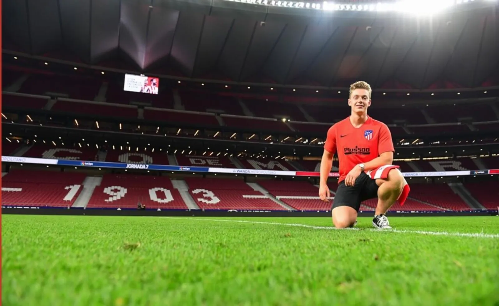Visitor kneeling on the Metropolitano pitch with 1903 in the seats behind